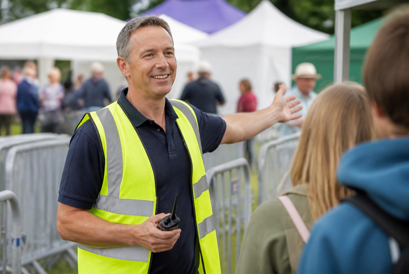 Friendly event steward in a hi-vis vest directing visitors at the entrance to a UK outdoor community festival